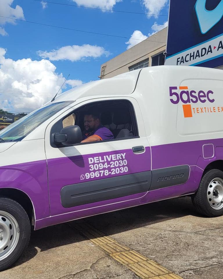 Utilitário da 5àsec com adesivagem roxa na metade inferior, a marca na lateral e os telefones do delivery na porta