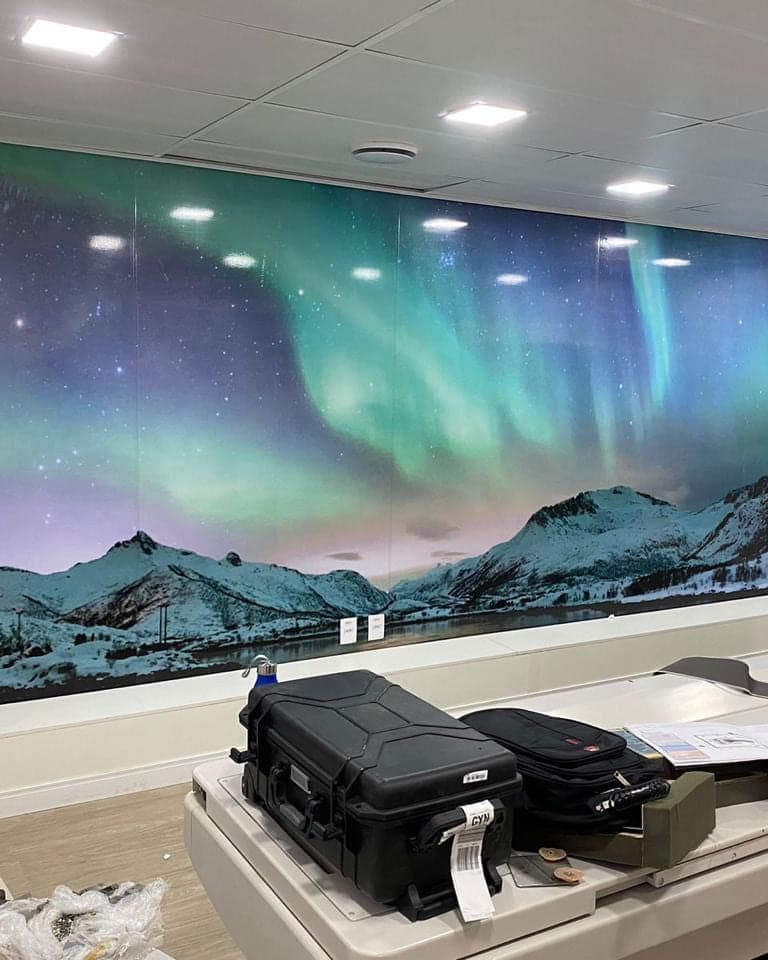 Parede de ambiente interno revestida de canto a canto com impressão de paisagem noturna com aurora boreal