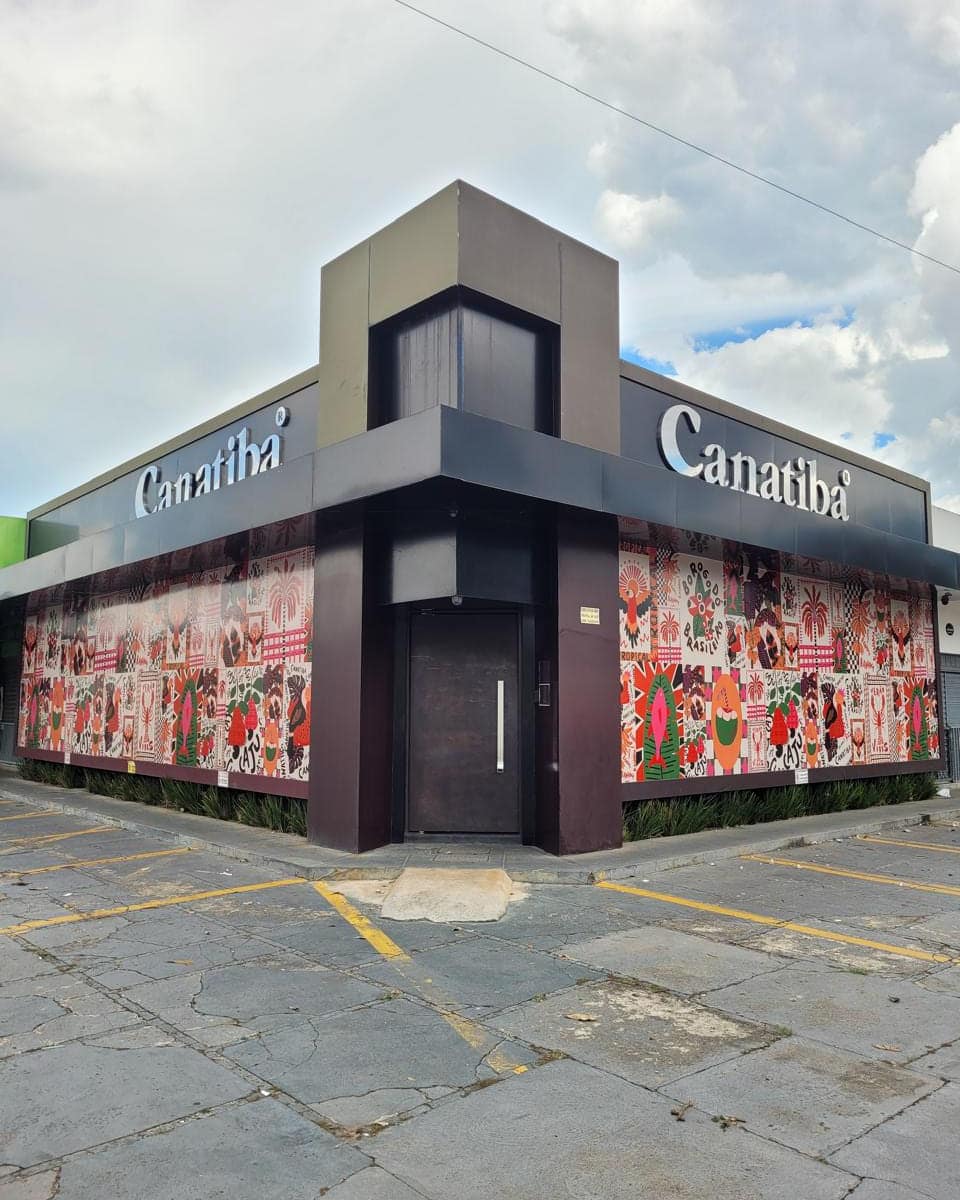 Loja de esquina da Canatibá com fachada em ACM escuro, a marca em letra caixa e as vitrines cobertas com adesivo impresso floral