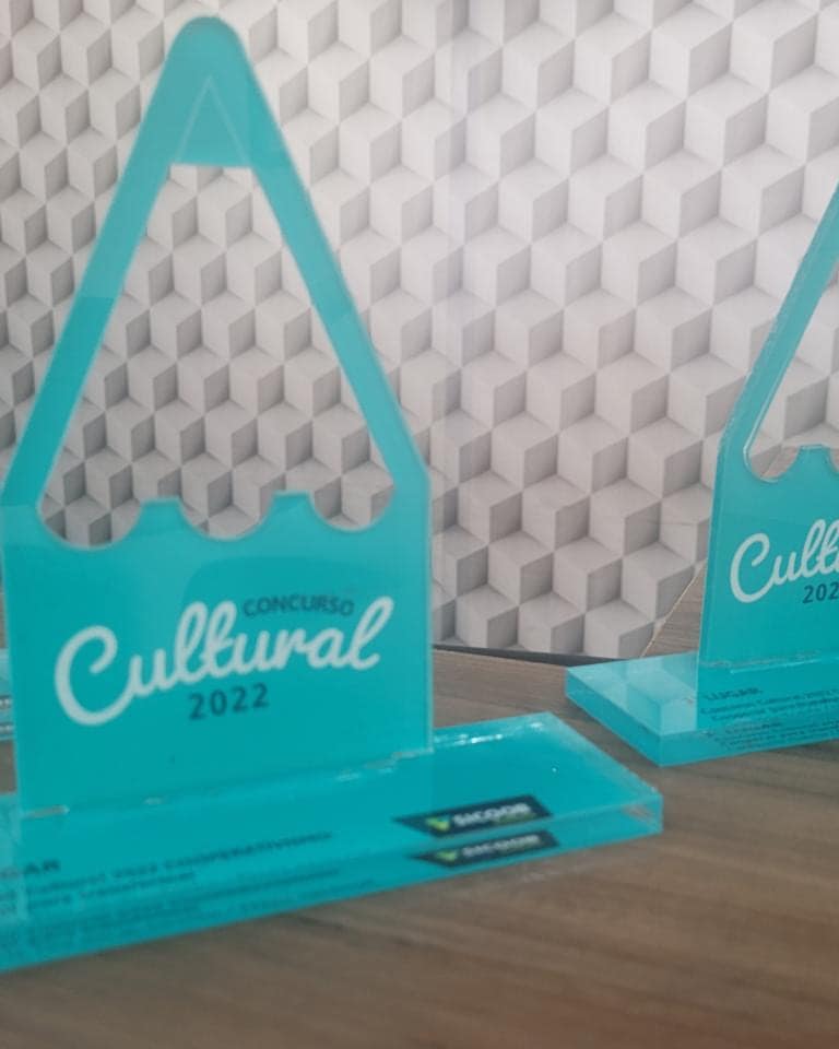 Troféus do Concurso Cultural 2022 em acrílico verde-água, recortados no formato de montanha, alinhados sobre a mesa