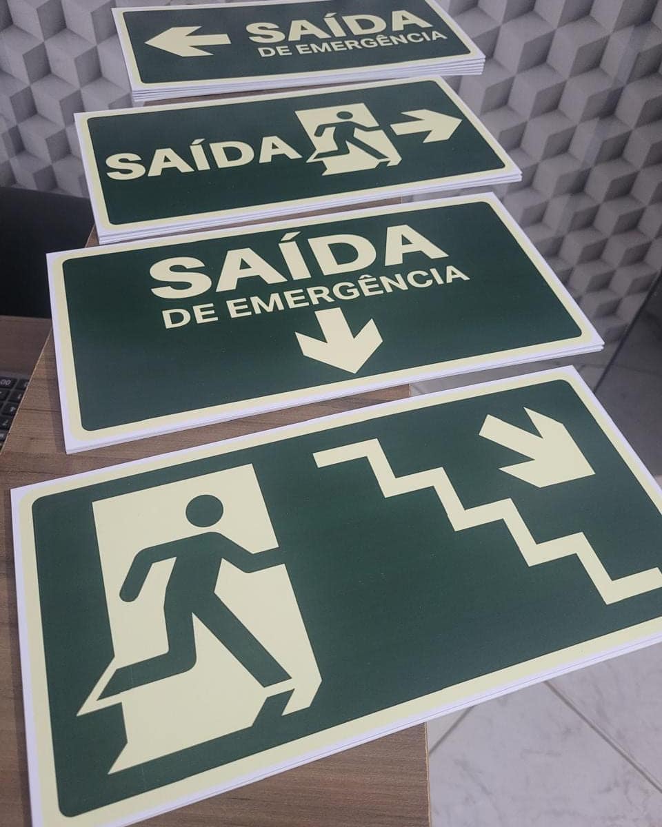 Pilhas de placas de saída de emergência em material fotoluminescente, com seta e pictograma