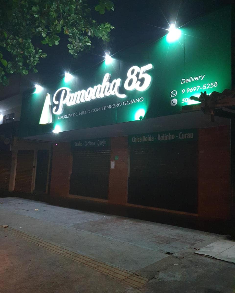 Fachada da Pamonha 85 à noite, com o letreiro em letra caixa iluminada sobre a testeira verde e spots acesos