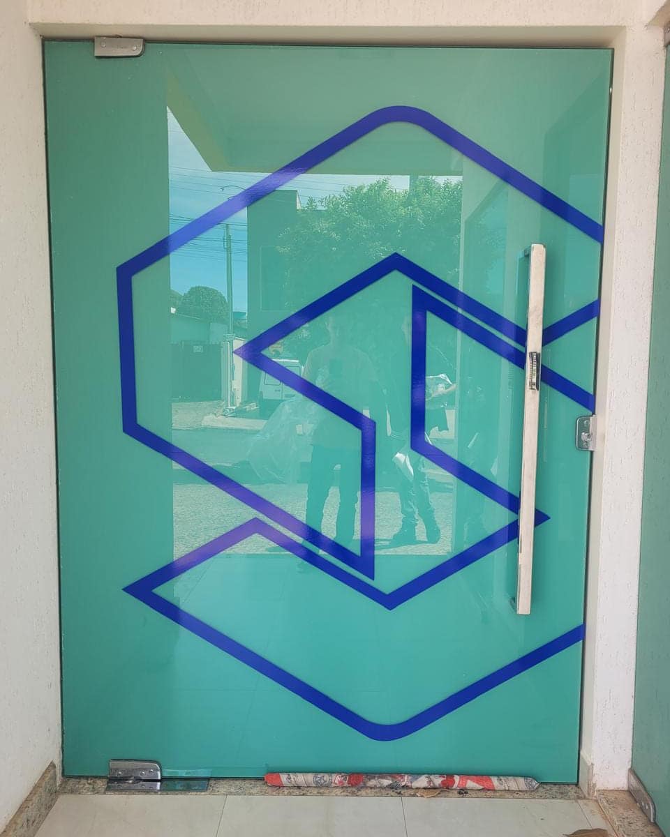 Porta de vidro com a marca em vinil azul recortado sobre fundo verde-água jateado