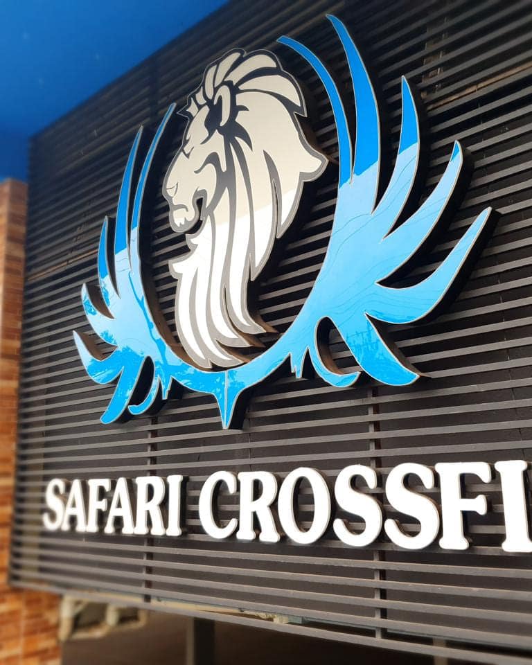 Letra caixa branca da Safari Crossfit sobre fachada metálica, com o símbolo do leão recortado em azul acima do nome