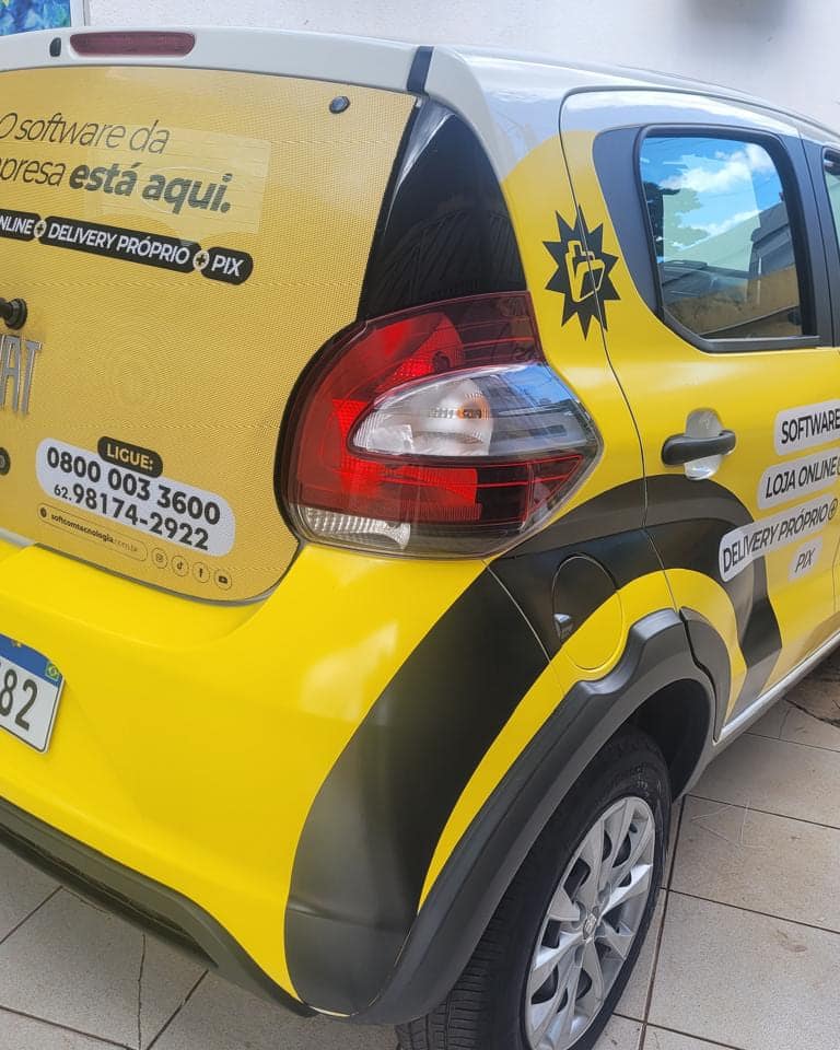 Carro compacto da Softcon envelopado em amarelo, com a chamada da empresa no vidro traseiro e a marca na lateral