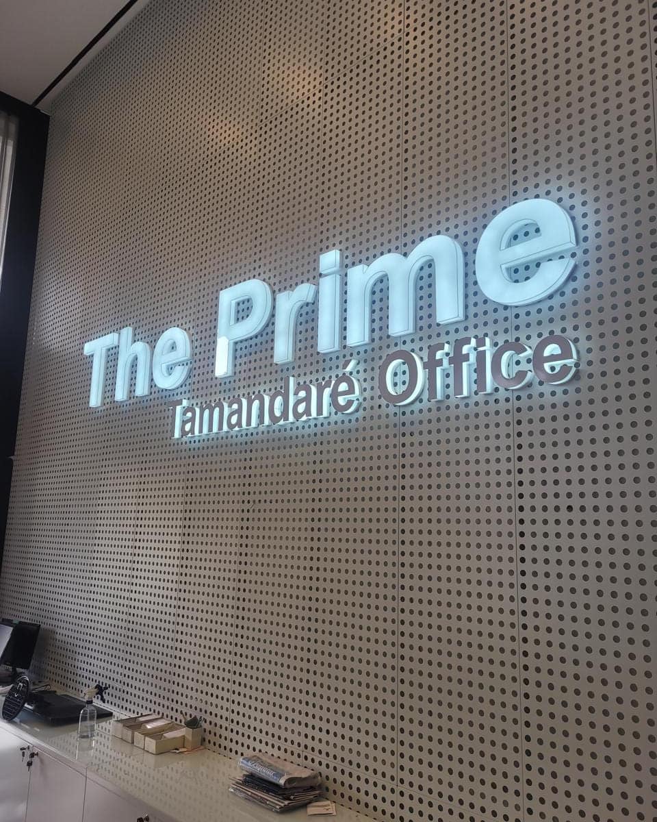 Letras da The Prime Tamandaré Office retroiluminadas sobre painel perfurado branco, na recepção do edifício