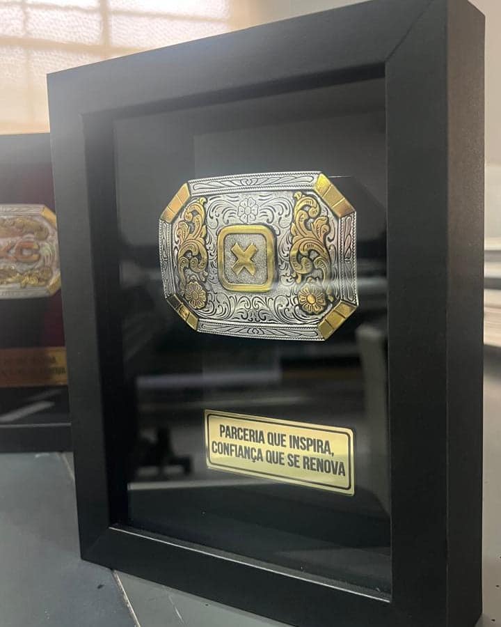 Quadro preto com fivela de cinto em relevo e placa dourada gravada, produzido para a TXC