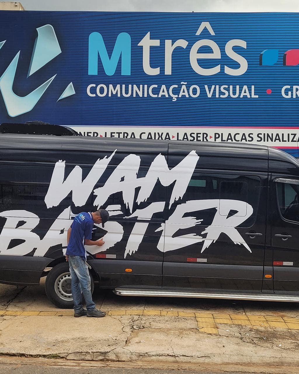 Van do artista Wam Baster envelopada em preto, com o nome em letras brancas, durante a aplicação na M3