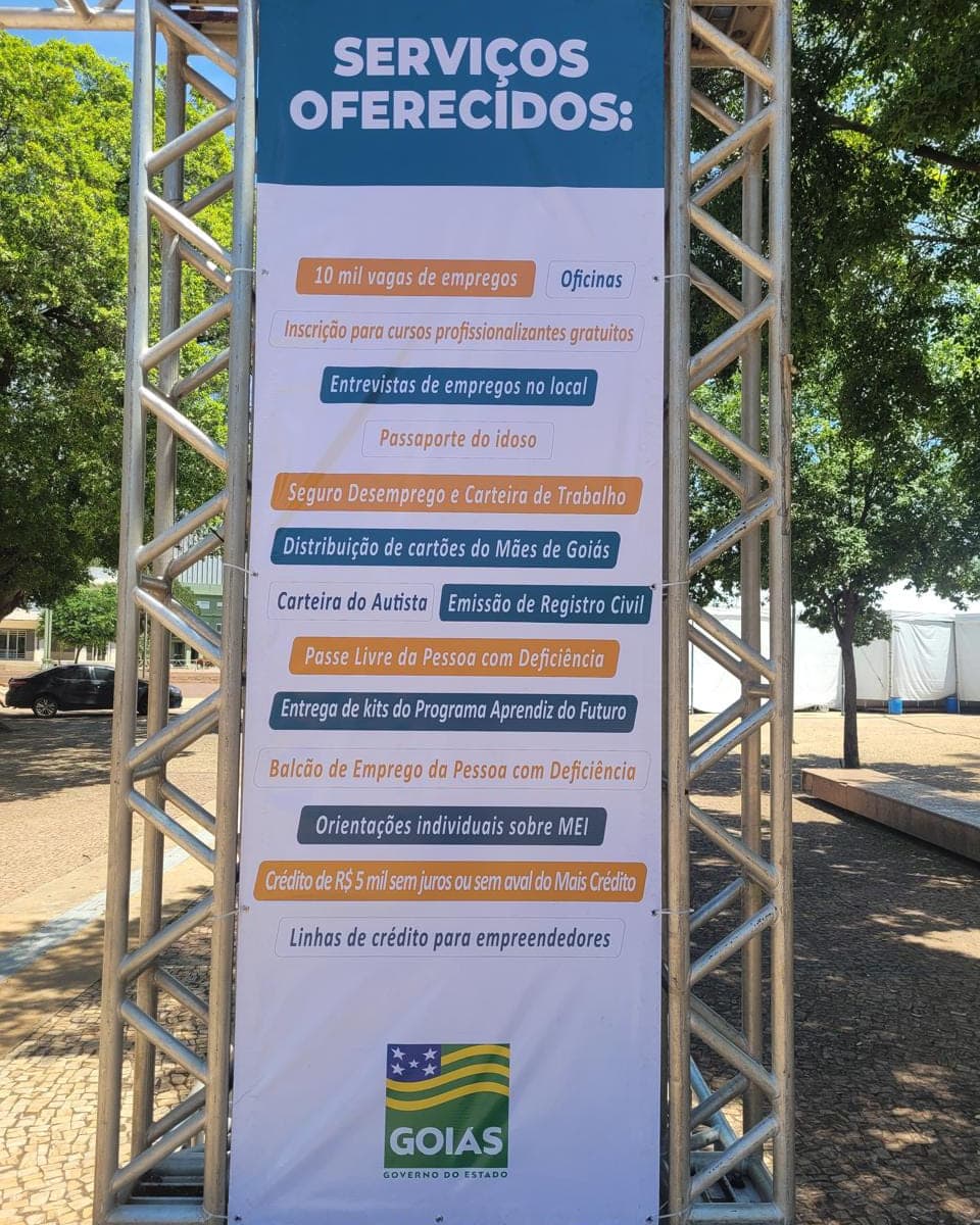 Banner em lona listando serviços oferecidos, com a marca do Governo de Goiás, esticado em estrutura de treliça ao ar livre