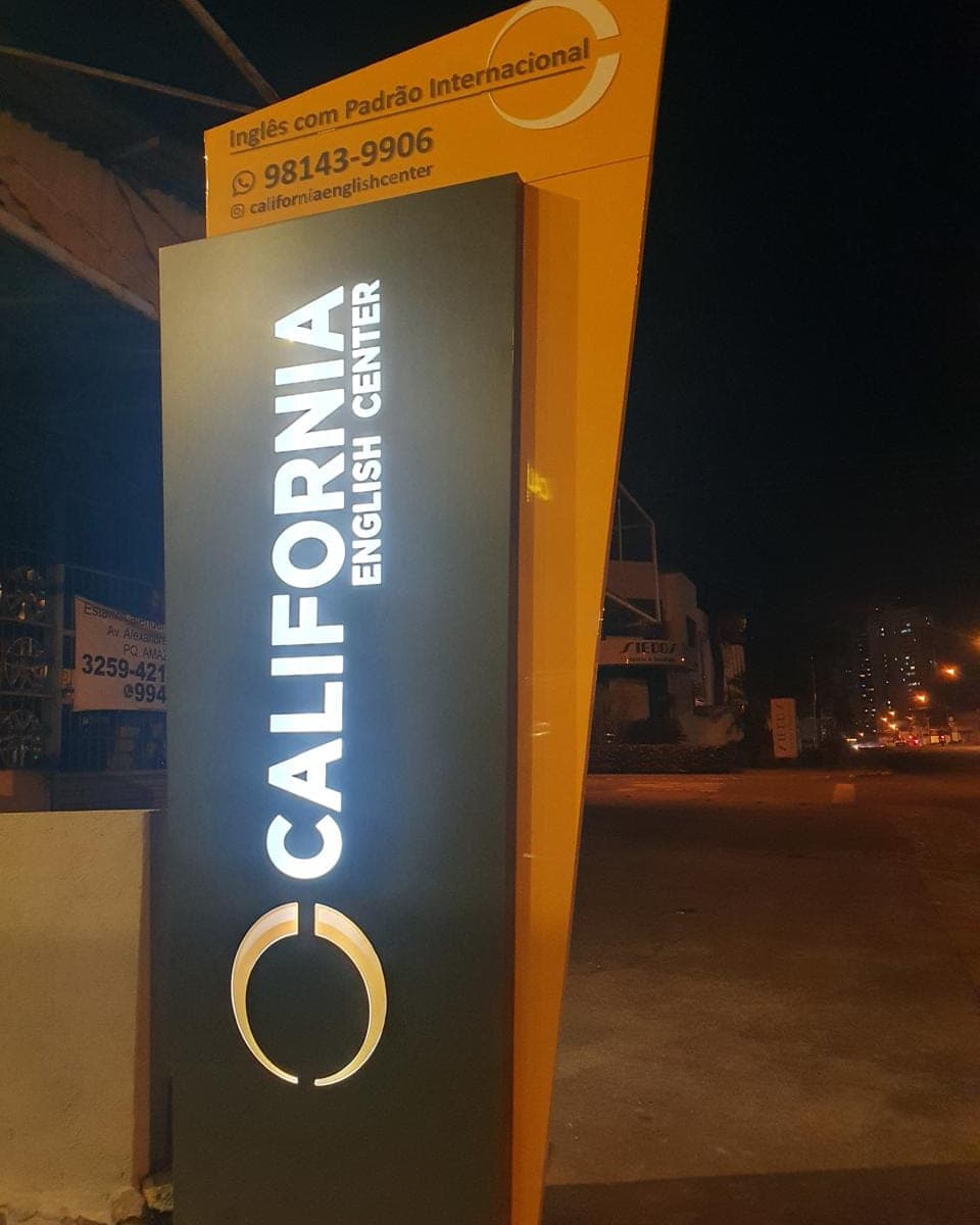 Totem da California English Center aceso à noite, em laranja e preto, com o nome iluminado na vertical