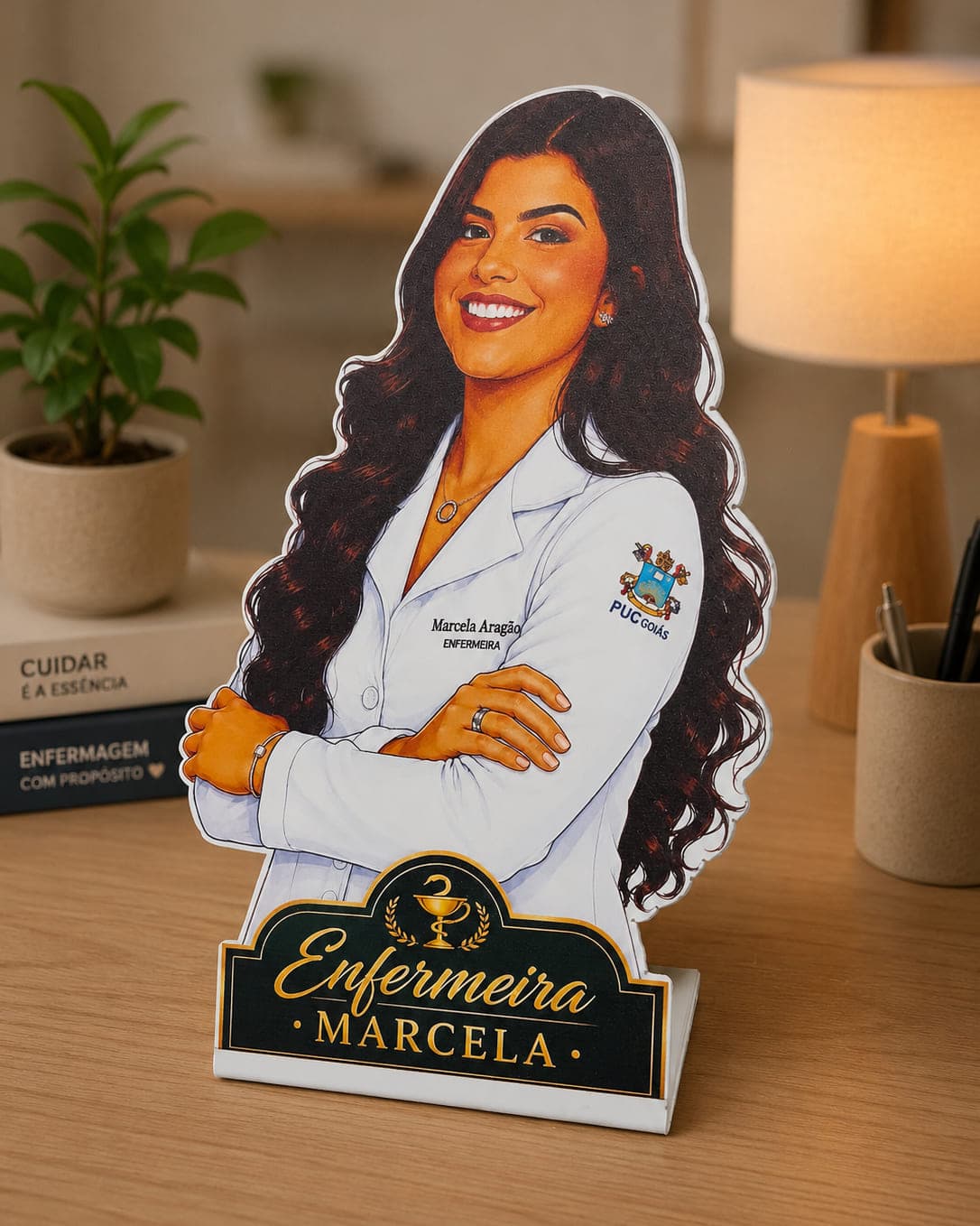 Display de mesa recortado com ilustração da enfermeira Marcela e placa dourada com o nome dela na base