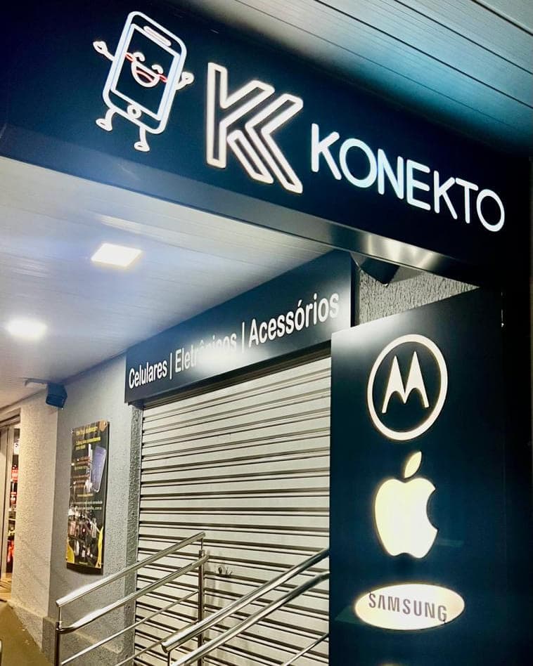 Fachada da Konekto à noite, com o letreiro iluminado no alto e as marcas que a loja vende aplicadas na lateral