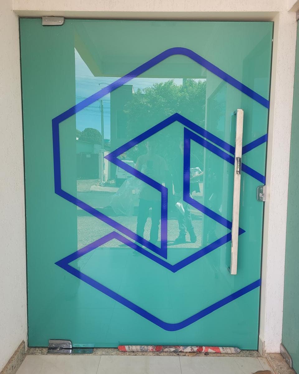 Porta de vidro com a marca em vinil azul recortado sobre fundo verde-água jateado