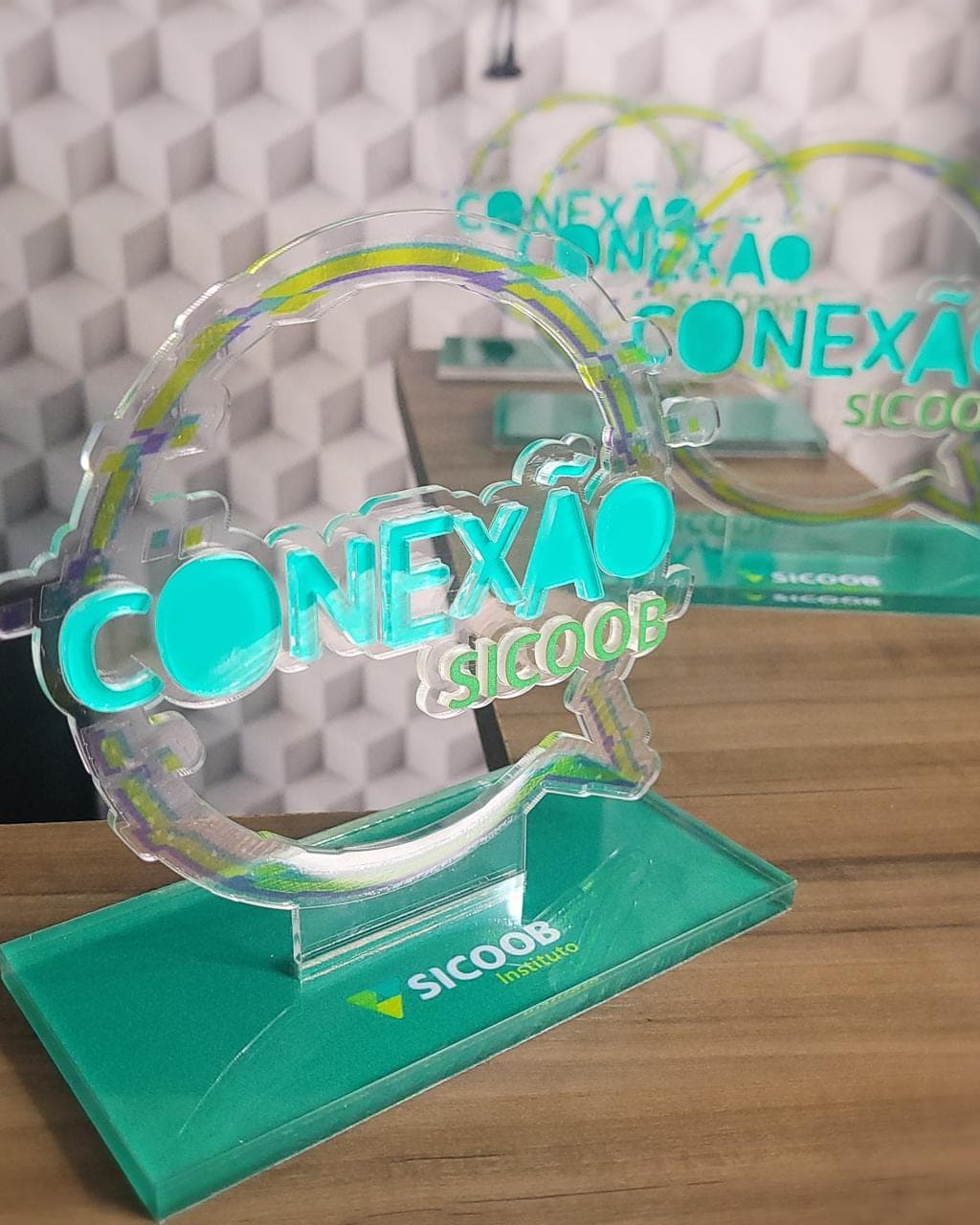 Troféu Conexão Sicoob em acrílico cristal com impressão em verde-água, sobre base em acrílico verde, com outros iguais ao fundo