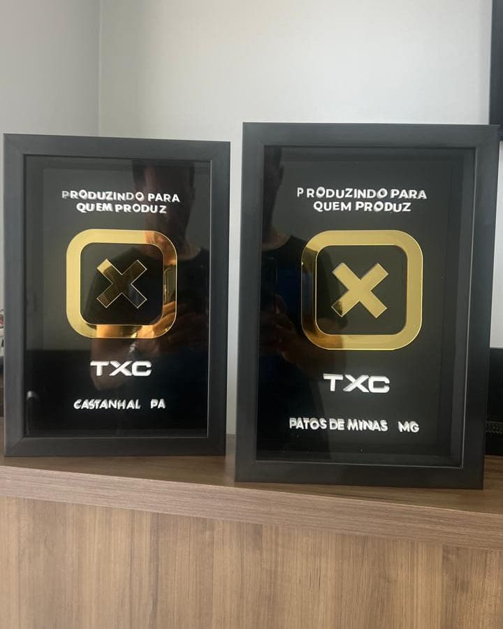 Placas de reconhecimento da TXC para revendas, em acrílico preto com o símbolo dourado e o nome da cidade de cada loja
