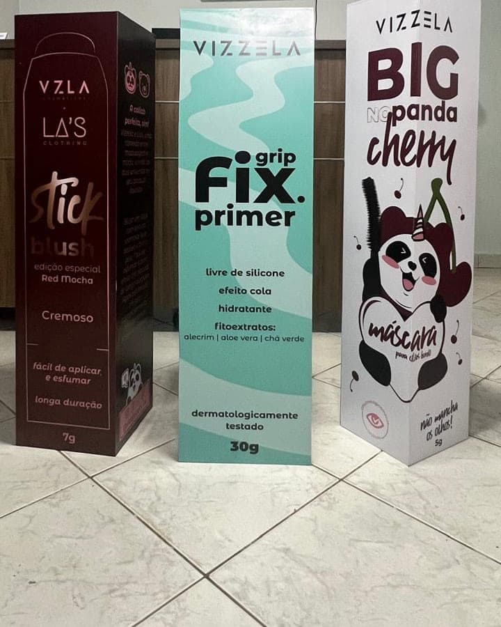 Três totens da Vizzela reproduzindo embalagens de cosmético em escala ampliada, lado a lado