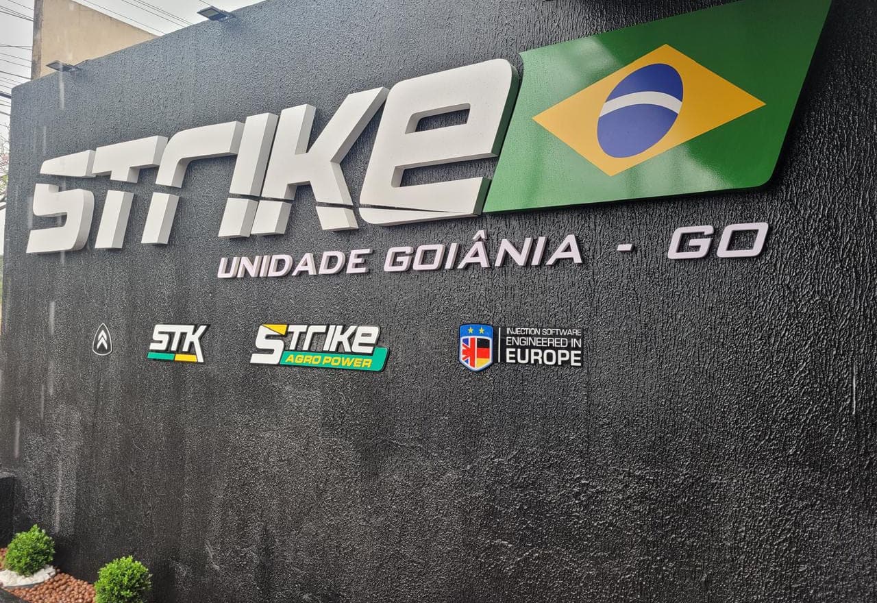 Letra caixa metálica da Strike aplicada sobre muro texturizado preto, com as submarcas alinhadas abaixo