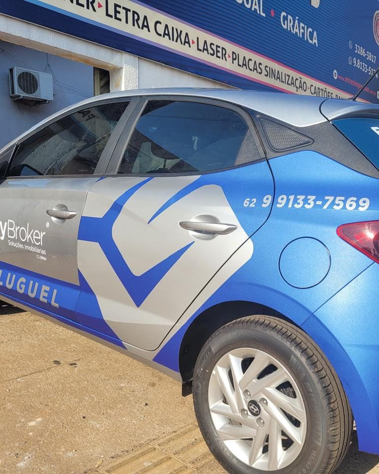 Lateral do carro da MyBroker envelopado em azul e prata, com a marca, o telefone e a palavra Aluguel na porta