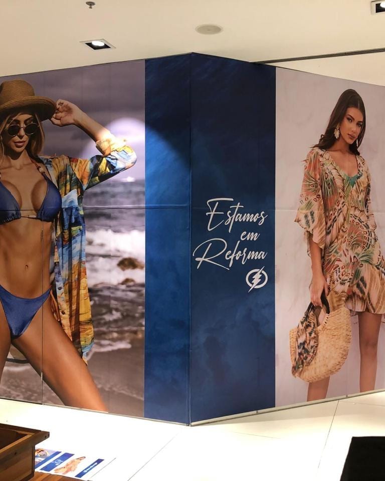 Tapume de loja em shopping revestido com impressão de campanha de moda e o aviso de reforma da Sol & Energia